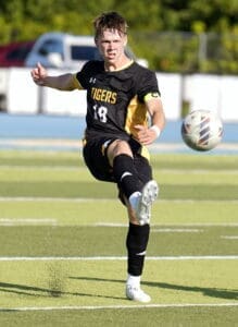 Soccer player in black uniform kicking the ball on a grassy field during an outdoor game, showcasing athleticism.