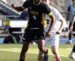 Soccer player in black jersey dribbles the ball past an opponent during an outdoor match on a sunny day.