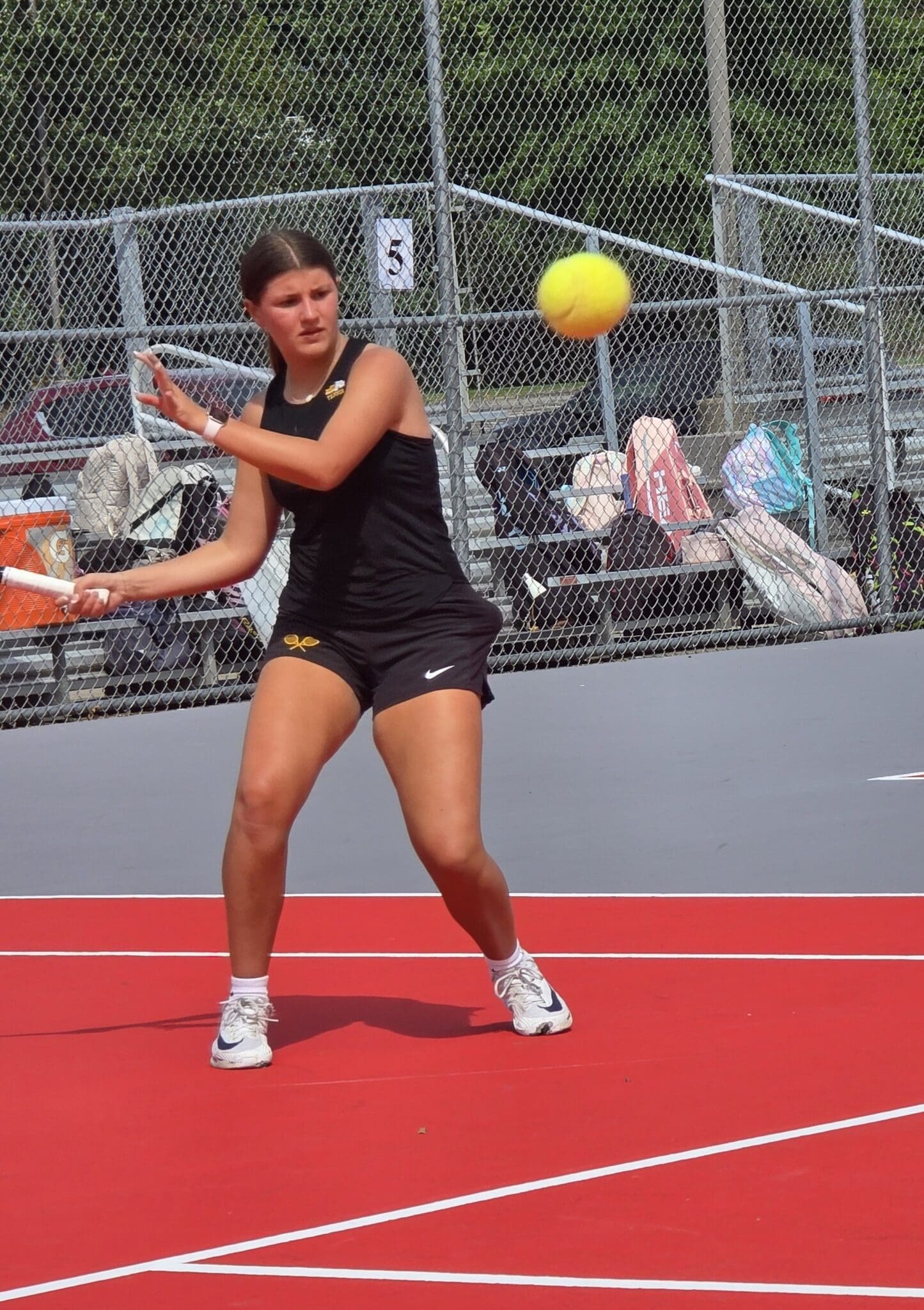 Tennis player poised to hit a yellow ball on a red court, showcasing athletic skill and focus during a match.