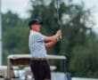 Young golfer swings a driver on the course, showcasing form and concentration amidst a backdrop of golf carts.