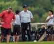 Four individuals at a golf course including a coach and players, discussing strategy near golf bags and equipment.