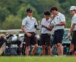 Four teenage golfers discuss strategy on the course, surrounded by golf bags and equipment. Focus on teamwork and sportsmanship.