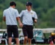 Two young golfers in matching striped shirts share a friendly moment on the course, with golf bags in the background.
