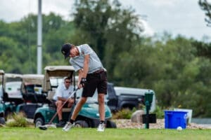 Young golfer in action, driving a ball on the fairway with golf carts in the background. Perfecting the swing technique.