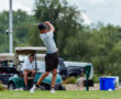 Young golfer preparing to hit a drive, with golf carts in the background on a lush green course.