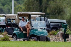 A man sitting in a golf cart on a lush green course, enjoying a sunny day at the golf club.