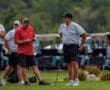 Group of golfers preparing for a game, with one checking his phone and others observing on a golf course.