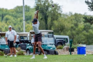 Young golfer preparing to swing a driver on the course, with golf carts visible in the background.