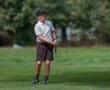 Young male golfer preparing to swing on a lush green golf course, dressed in a striped shirt and shorts.