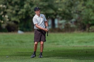 Young male golfer preparing to swing on a lush green golf course, dressed in a striped shirt and shorts.
