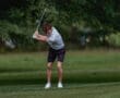 A young golfer swings a club on a lush green fairway, showcasing focus and athleticism in a natural setting.
