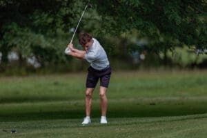A young golfer swings a club on a lush green fairway, showcasing focus and athleticism in a natural setting.