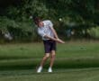 A golfer in a striped shirt swings a club on a green course, showcasing skill and focus in a natural setting.