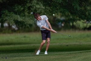 A golfer in a striped shirt swings a club on a green course, showcasing skill and focus in a natural setting.
