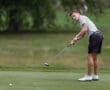 Young male golfer putting on a green, focused on the ball, wearing a striped shirt and black shorts.