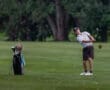 A golfer swings a club on a lush green course, with a golf bag nearby and grass flying from the impact.