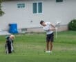 Young golfer swinging a club on a lush green course, with golf clubs and a plush toy in the background.