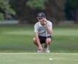 Young golfer crouches down on the green, focusing intently on his putt. Perfect summer day for a game of golf.