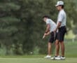 Two young golfers focus intently on the green, preparing to putt during a sunny day at a golf course.