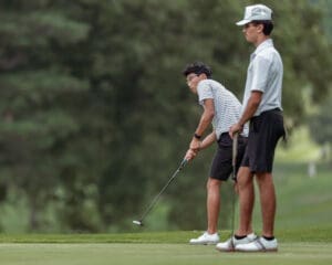 Two young golfers focus intently on the green, preparing to putt during a sunny day at a golf course.