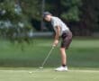 Young golfer in a striped shirt putts on a green golf course, focusing intently on the ball.