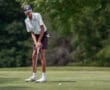 Young golfer in striped shirt preparing to putt on the green against a lush backdrop, focusing intently before the shot.