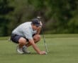 Young golfer kneels on the green, preparing to putt, focused on the ball with a putter in hand.