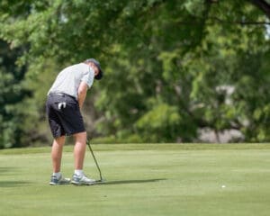 Golfer focusing on putting on a sunny day, surrounded by lush greenery on the course.
