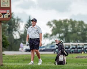 Young golfer walking on the course, carrying a golf bag, prepares for his next shot under a cloudy sky.