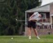 A golfer in a striped shirt swings at a golf ball on the course, with grass flying in the air.