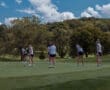 Team of young female golfers practicing putting on a sunny course with lush greenery and a blue sky overhead.