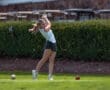 A golfer swings a club on the course, focusing on her technique with a lush green background.