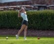 A young woman tees off on a sunny golf course, preparing to drive the ball into the distance.