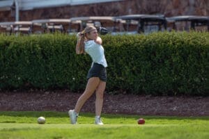 A young woman tees off on a sunny golf course, preparing to drive the ball into the distance.