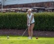 Young woman preparing to tee off on a golf course, with golf balls and lush greenery in the background.