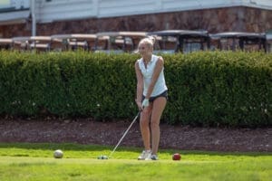 Young woman preparing to tee off on a golf course, with golf balls and lush greenery in the background.
