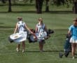 Two young female golfers walking on a lush course, carrying bags and preparing for a round of golf.