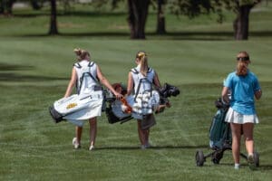 Two young female golfers walking on a lush course, carrying bags and preparing for a round of golf.