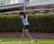 A young girl in a blue shirt and shorts swinging a golf club on a green course with colorful balls nearby.