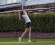 A young girl swings a golf club on the green, preparing to hit a ball at a golf course.