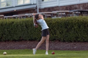 A young girl swings a golf club on the green, preparing to hit a ball at a golf course.