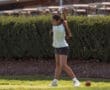 Young girl practicing her golf swing on a sunny day, focusing on technique with golf balls visible nearby.