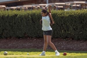 Young girl practicing her golf swing on a sunny day, focusing on technique with golf balls visible nearby.