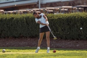 Young woman swinging a golf club on a lush green course, ready to make a perfect shot.