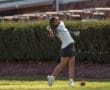 Young female golfer swinging a driver on the course, surrounded by greenery, showcasing athletic skill and focus.