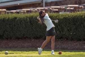 Young female golfer swinging a driver on the course, surrounded by greenery, showcasing athletic skill and focus.