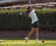 A young woman tees off on a golf course, showcasing her swing against a lush green backdrop.