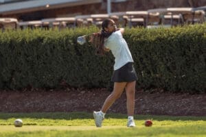 A young woman tees off on a golf course, showcasing her swing against a lush green backdrop.