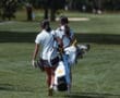 Two young girls walking on a golf course, carrying golf bags under sunny skies, showcasing youth sports enthusiasm.
