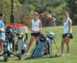 Three female golfers in casual attire gather on the course, discussing their game while surrounded by golf bags.